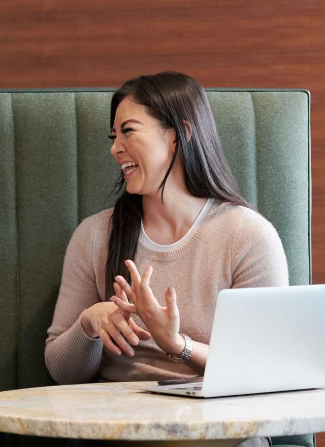 Two women sitting next to each other smiling and laughing in an office setting