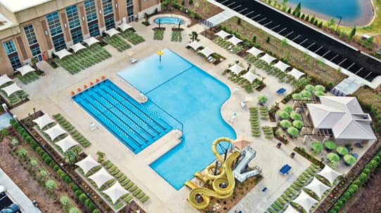 A aerial view of a Life Time outdoor pool with waterslides and lap pool along with lounge chairs
